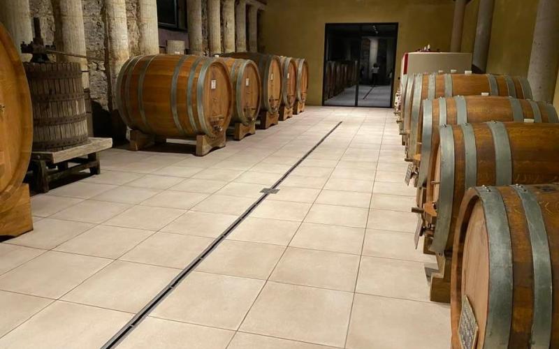 Pavimento in grès chiaro per cantina vinicola con botti in legno